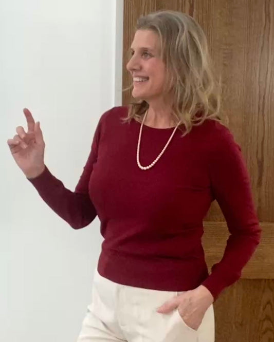 Woman wearing a red sweater and white pants in a room with wooden doors and a white wall.