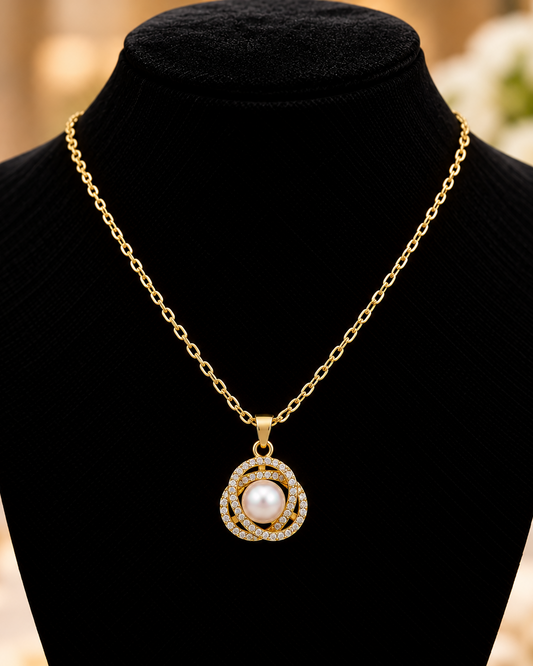 A gold chain necklace with a circular pendant featuring a central white pearl and surrounding clear stones, displayed on a black jewelry bust.