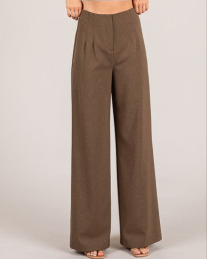Woman wearing a white crop top and brown wide-leg pants on a plain background