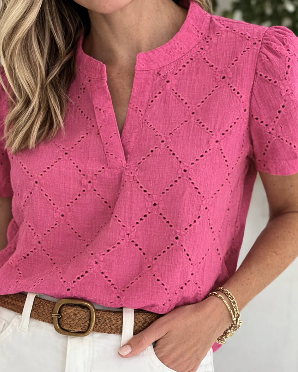 Woman wearing a pink blouse with a diamond pattern, white pants, and a brown belt.
