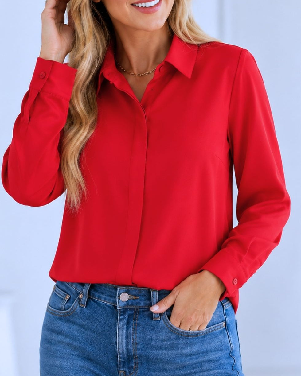 A woman wearing a bright red long-sleeve button-up shirt tucked into blue jeans, shown from the chest down against a light blue background.