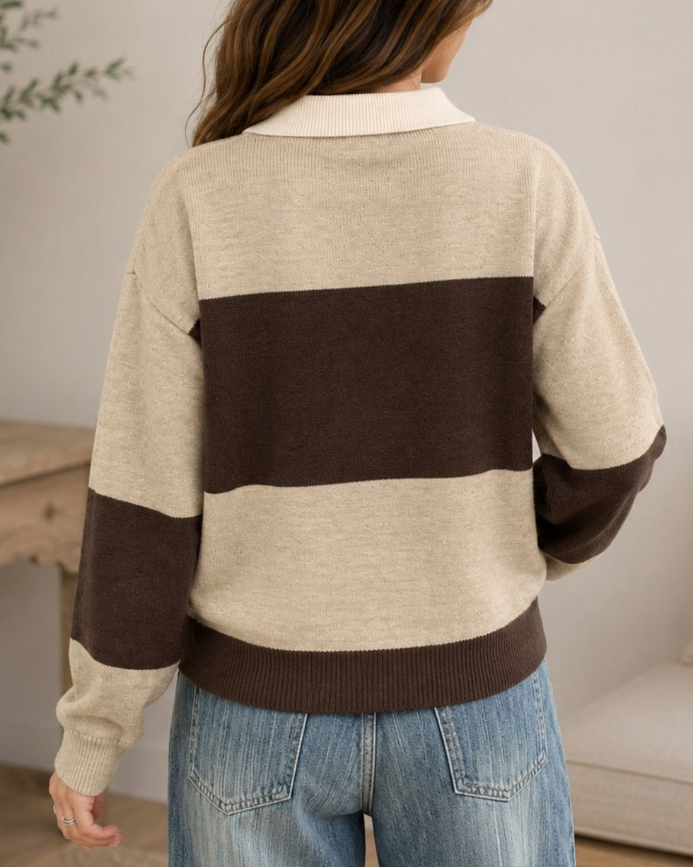 A woman shown from the back wearing a color-block knit sweater with a cream base and a wide dark brown horizontal stripe across the upper back and shoulders. The sweater has a cream ribbed collar, cream upper sleeves, and dark brown lower sleeves, hem, and shoulder panels, paired with blue jeans.