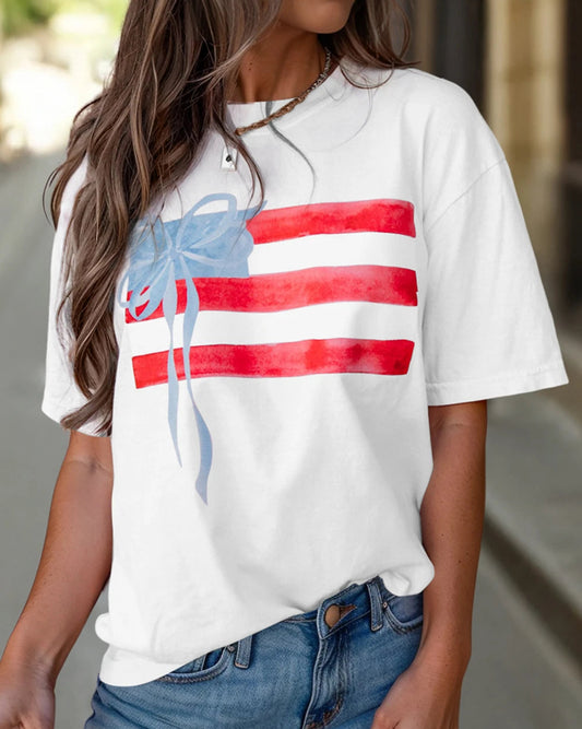 Person wearing a white t-shirt with a red, white, and blue graphic design outdoors.