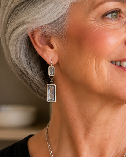 Woman with gray hair wearing a black top and necklace in a home setting