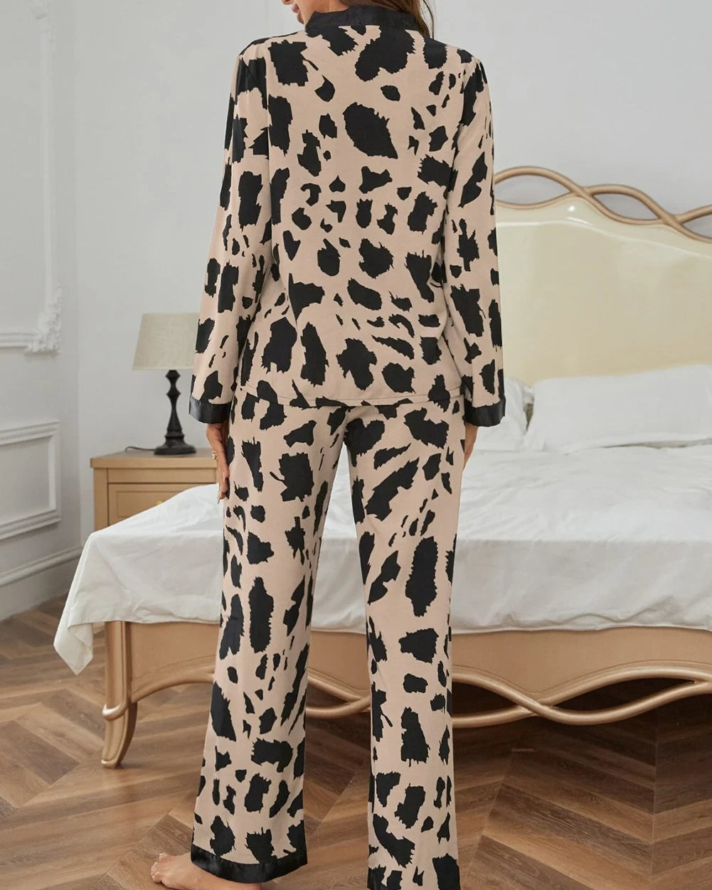 Woman wearing a leopard print pajama set in a bedroom.