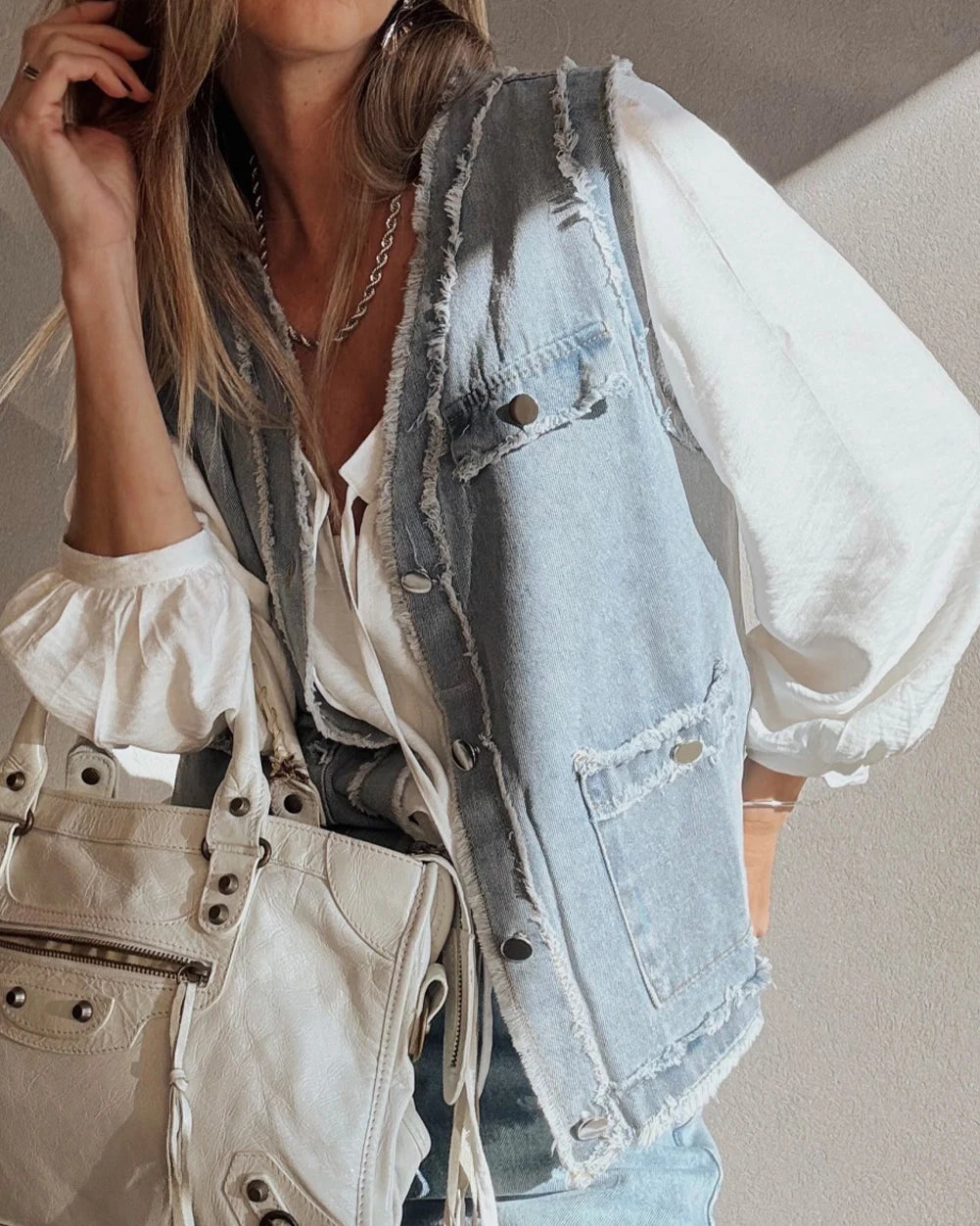 Woman wearing a light blue denim vest over a white blouse with a neutral background