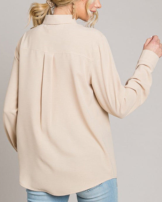 Woman wearing a beige long-sleeve shirt and blue jeans on a gray background