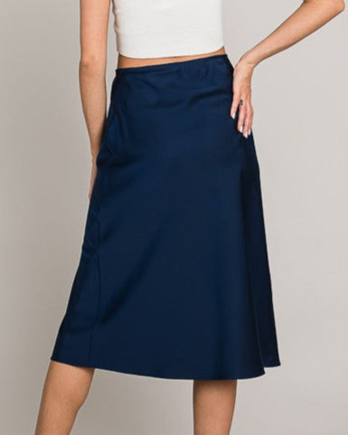 Woman wearing a white top and navy skirt on a plain background