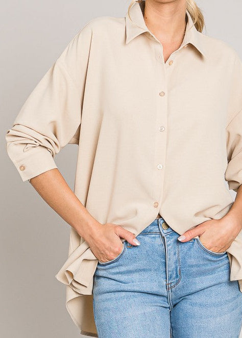 Woman wearing a beige button-up shirt and blue jeans against a plain background