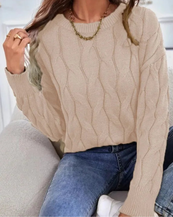 Person wearing a beige cable knit sweater and blue jeans sitting on a white couch.