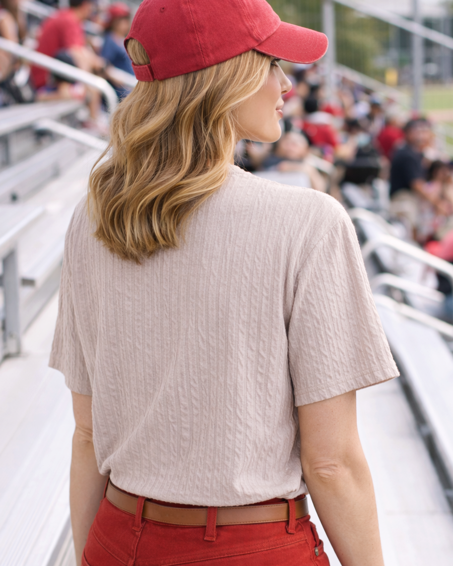 Woman wearing a red cap and red pants sitting in bleachers with a crowd in the background