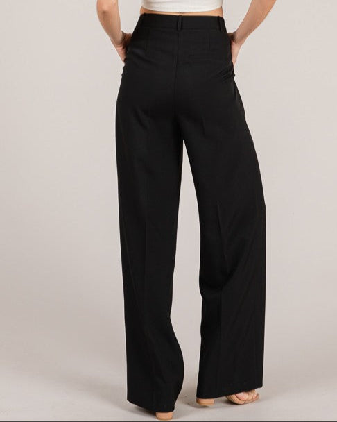 Woman wearing a white top and black high-waisted pants on a plain background