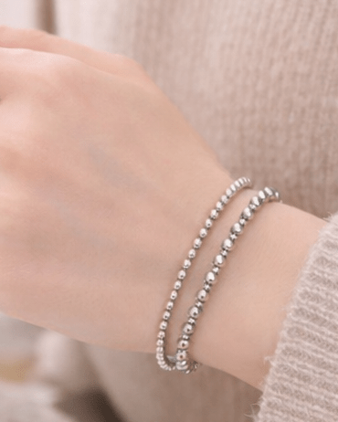 Hand wearing a bracelet and ring, holding a white mug.