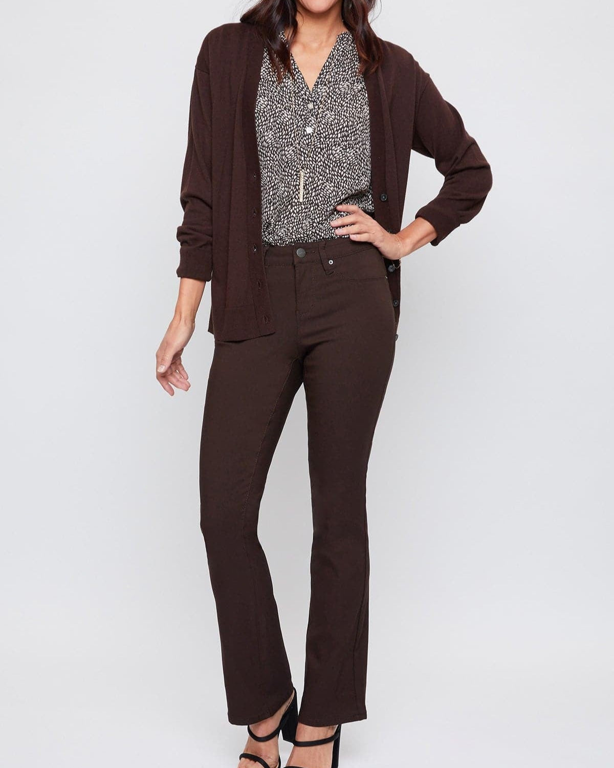 Woman wearing a brown cardigan, patterned blouse, and dark pants on a white background