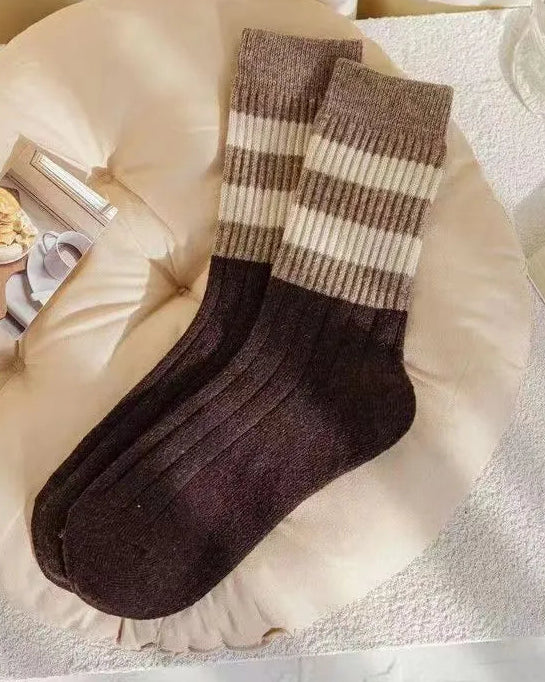Pair of brown and beige striped socks on a white surface with a book and glass in the background.