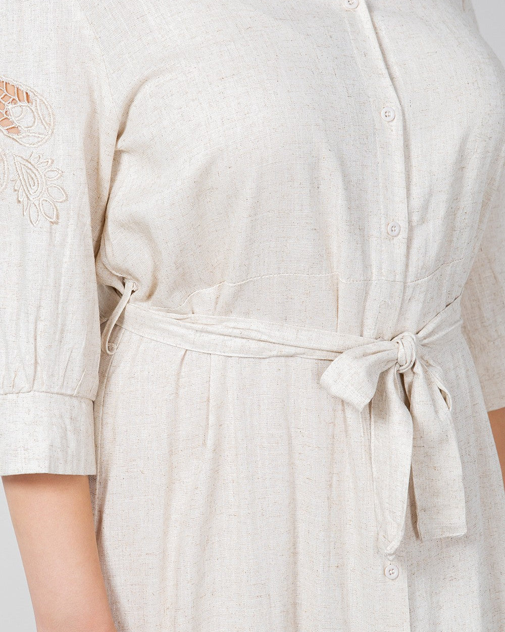 Close-up of a person wearing a light-colored dress with lace details on a plain background
