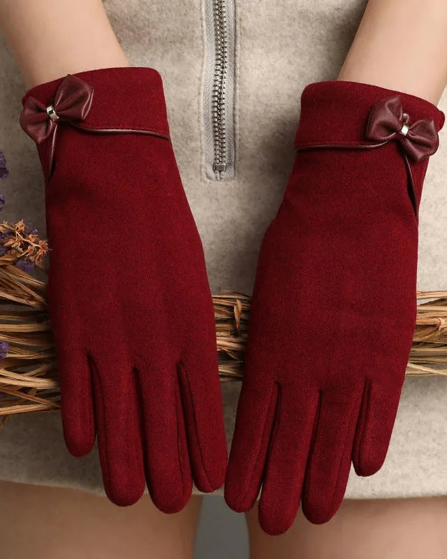 A pair of women's long gloves in deep burgundy red, featuring a matching fabric bow with a small rhinestone center on the back cuffs. The gloves are shown being worn on hands, styled with dried purple flowers and a beige knit sweater.