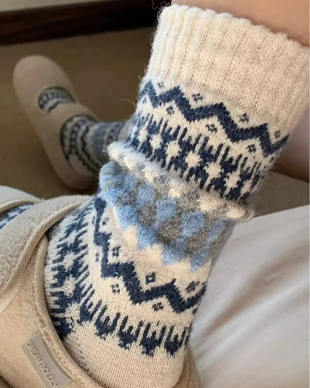 Close-up of feet wearing patterned socks and slippers on a soft surface.