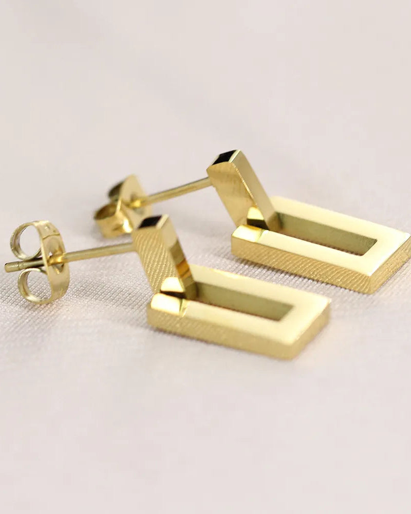 Gold rectangular stud earrings on a light background