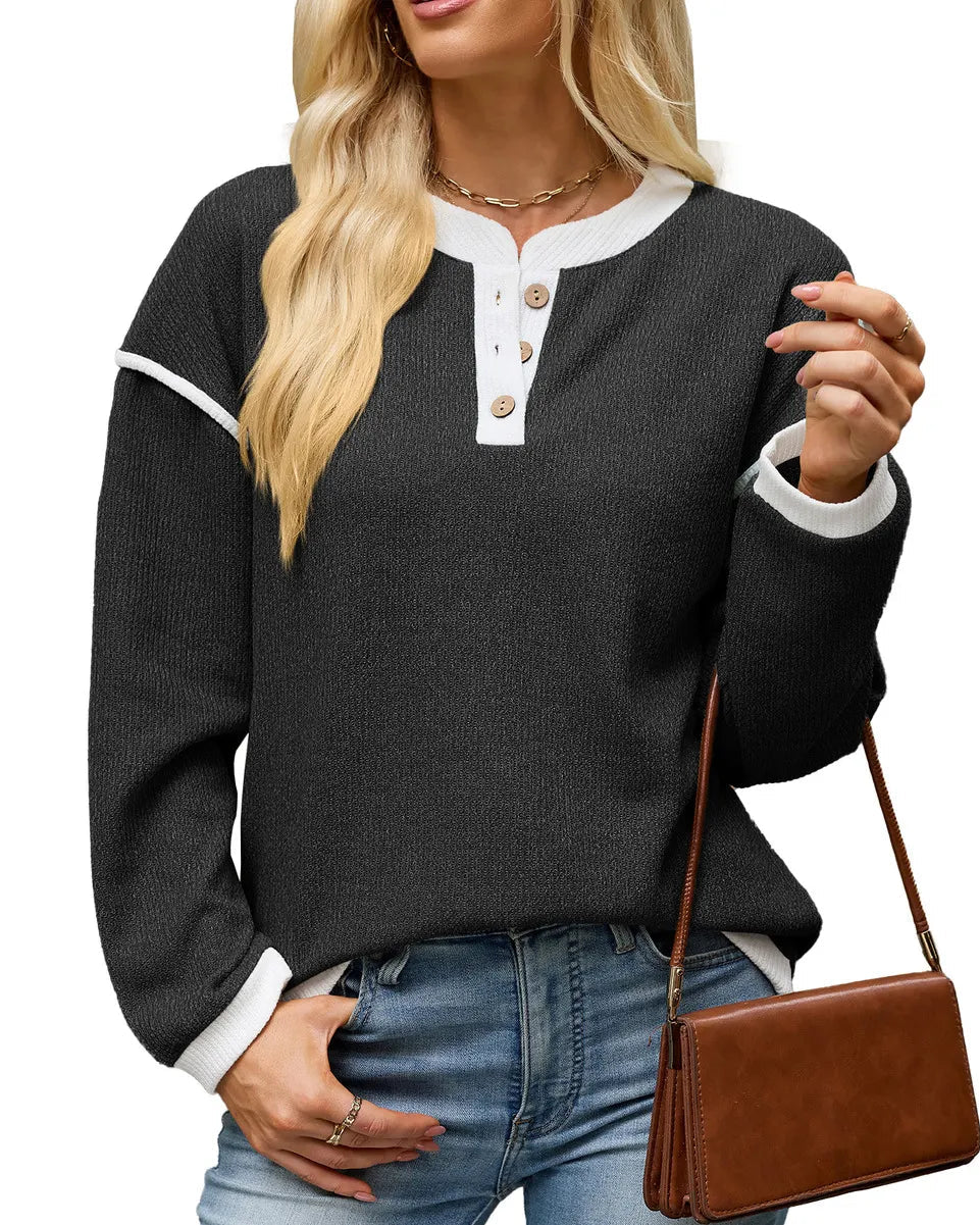 A woman wearing a dark gray ribbed Henley sweater with white contrast trim and buttons, paired with blue jeans and holding a brown crossbody bag, against a plain white background.