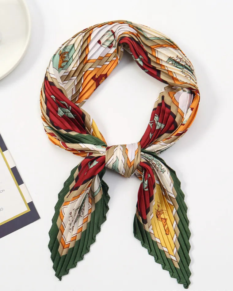 A pleated silk scarf with a multicolor vintage map print, tied in a knot and displayed on a clean white surface alongside a small card and a white plate.