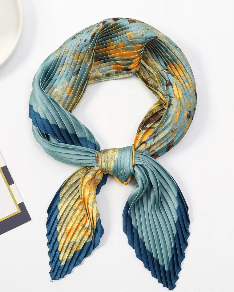 A pleated silk scarf with a blue, teal, and orange abstract pattern, tied in a knot and displayed on a clean white surface.