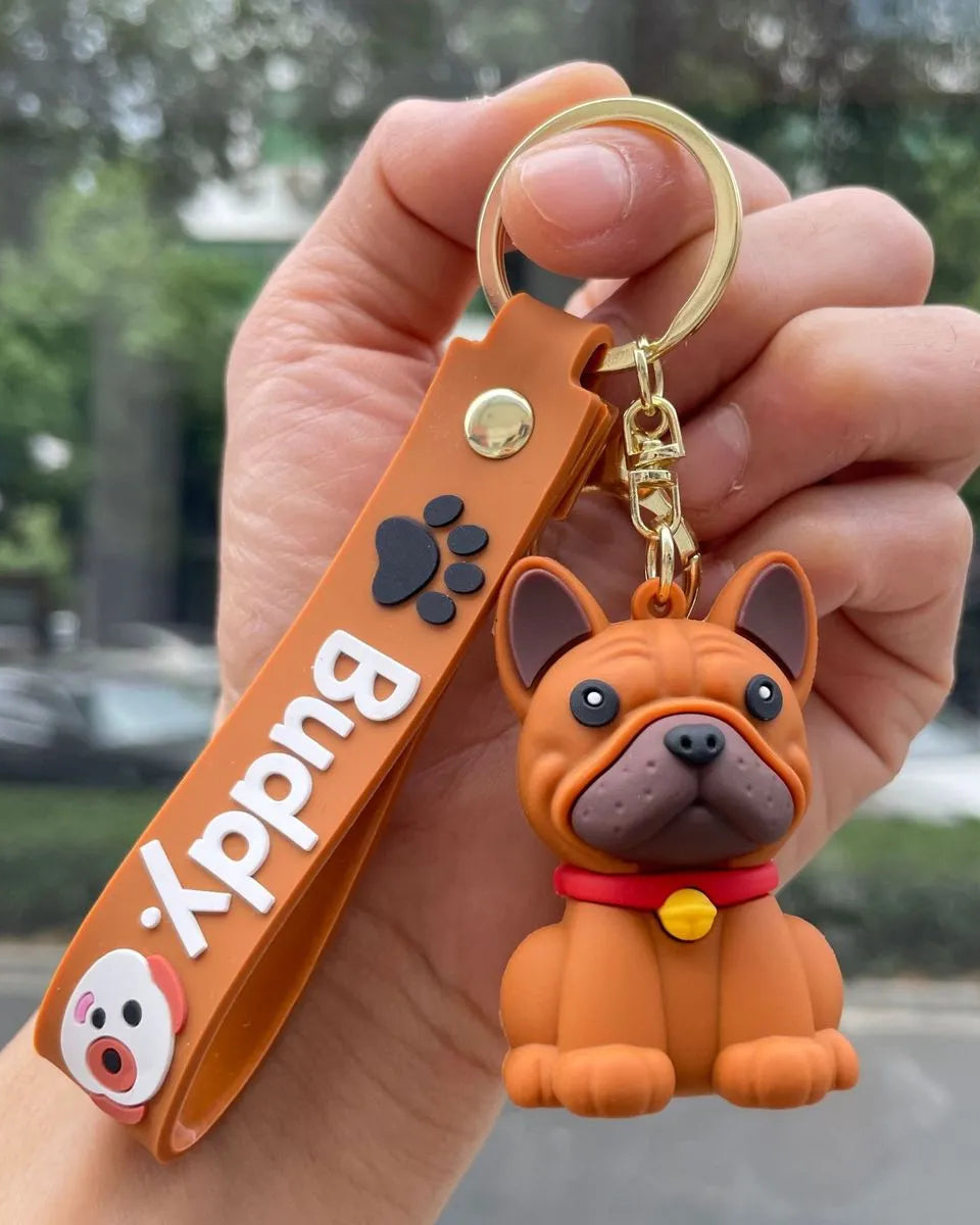 Hand holding a keychain with a dog figure and 'Buddy' tag, outdoors.