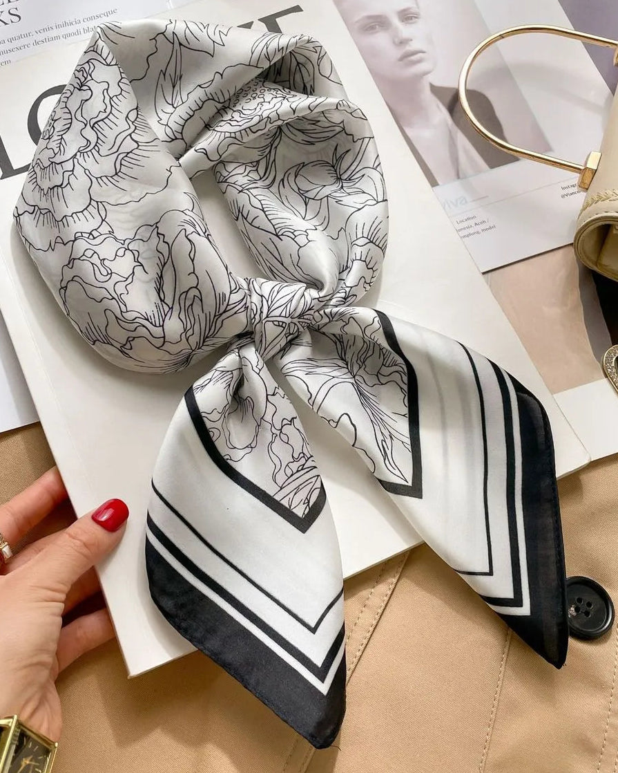 Black and white patterned scarf held by a hand on top of a magazine with a beige handbag.