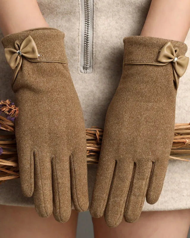 Brown gloves with decorative bows held by a person against a neutral background