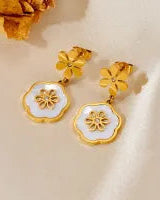 Gold earrings with white floral designs on a light background