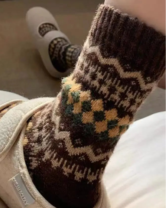 Person wearing brown patterned socks with a white slipper on a light background