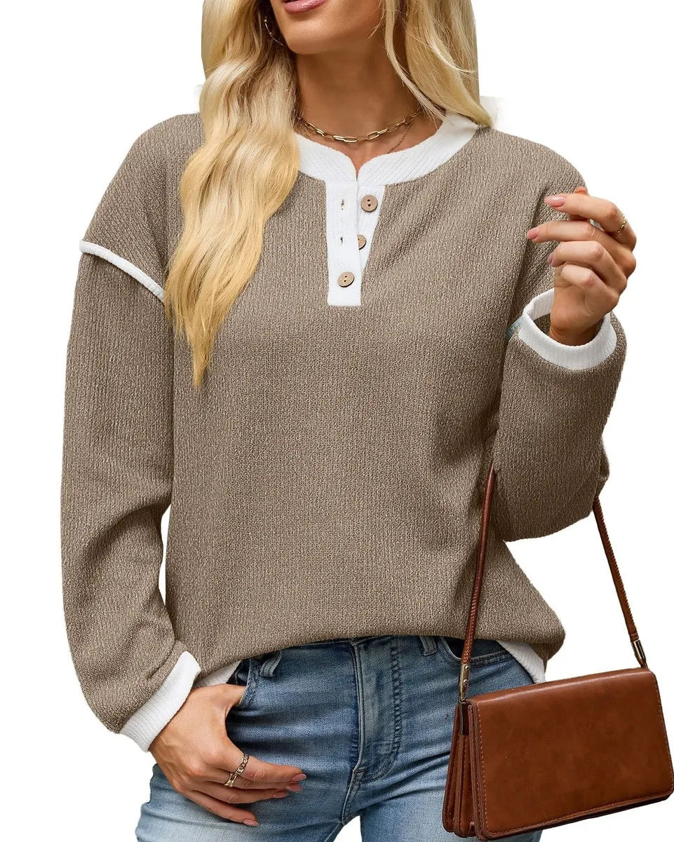 A woman wearing a taupe-brown long-sleeve henley sweater with white ribbed trim and buttons, paired with blue jeans and holding a brown crossbody bag, against a plain white background.