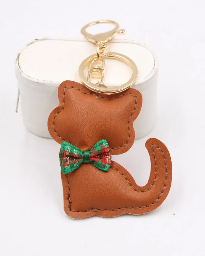 A brown faux-leather cat-shaped keychain with a green and red plaid bow accent, attached to gold-tone metal rings, shown against a white background.