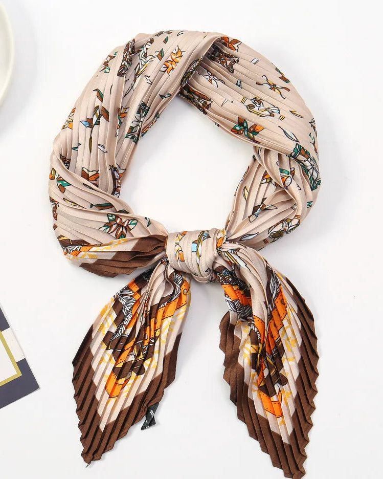 A pleated silk scarf with a beige, brown, and orange floral pattern, tied in a knot and displayed on a clean white surface.