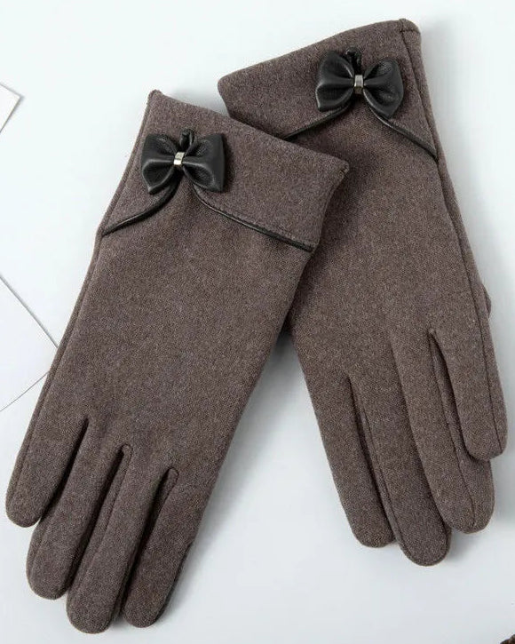 Pair of brown gloves with black bow details on a white surface