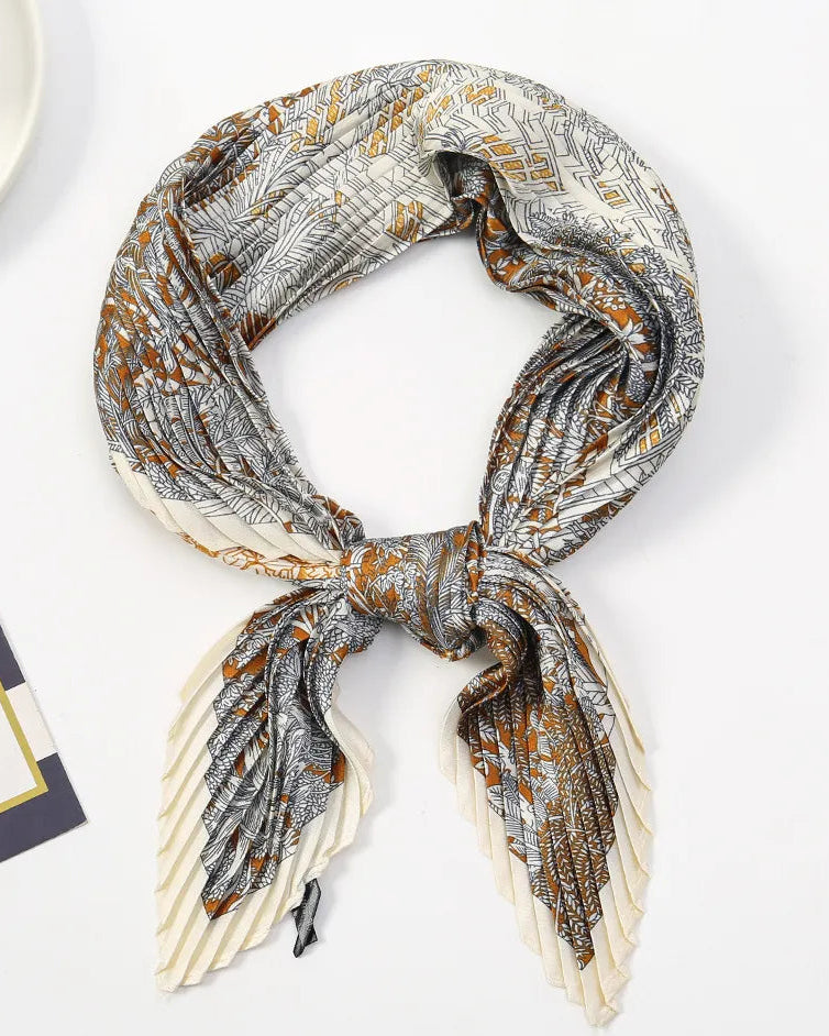 A pleated silk scarf with a gray, white, and brown abstract pattern, styled in a loop with a knot at the center on a white background.