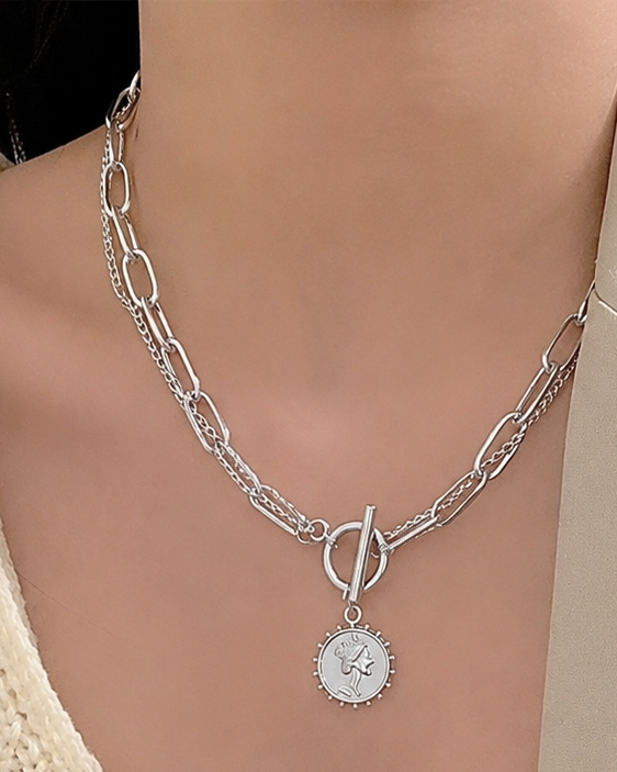 Silver necklace with a pendant worn by a person in a beige outfit.