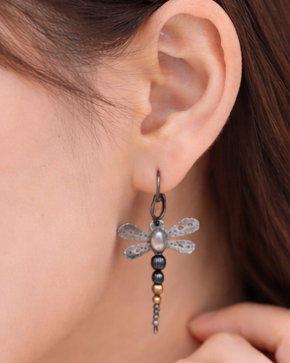Close-up of an ear wearing a dragonfly-shaped earring with a pearl center.