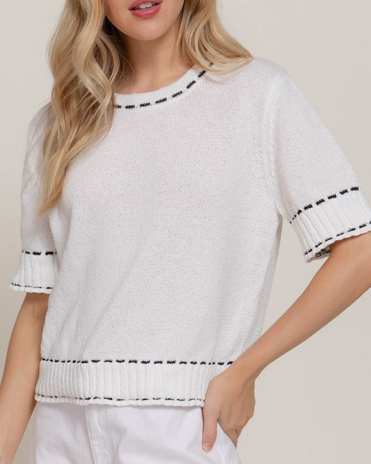 Woman wearing a white sweater with black trim on a plain background