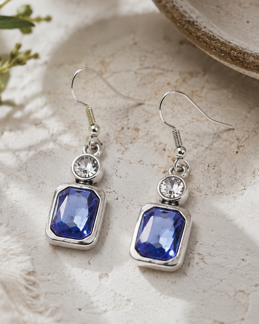Pair of blue gemstone earrings with silver hooks on a textured surface.
