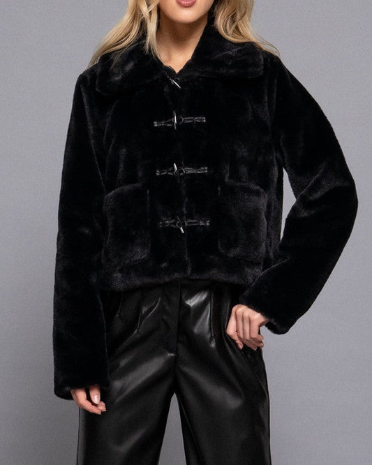 Woman wearing a black faux fur jacket and black pants on a gray background