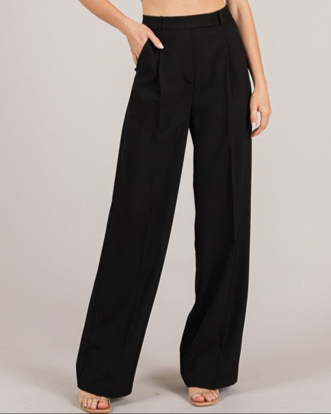 Woman wearing a white crop top and black wide-leg pants on a plain background