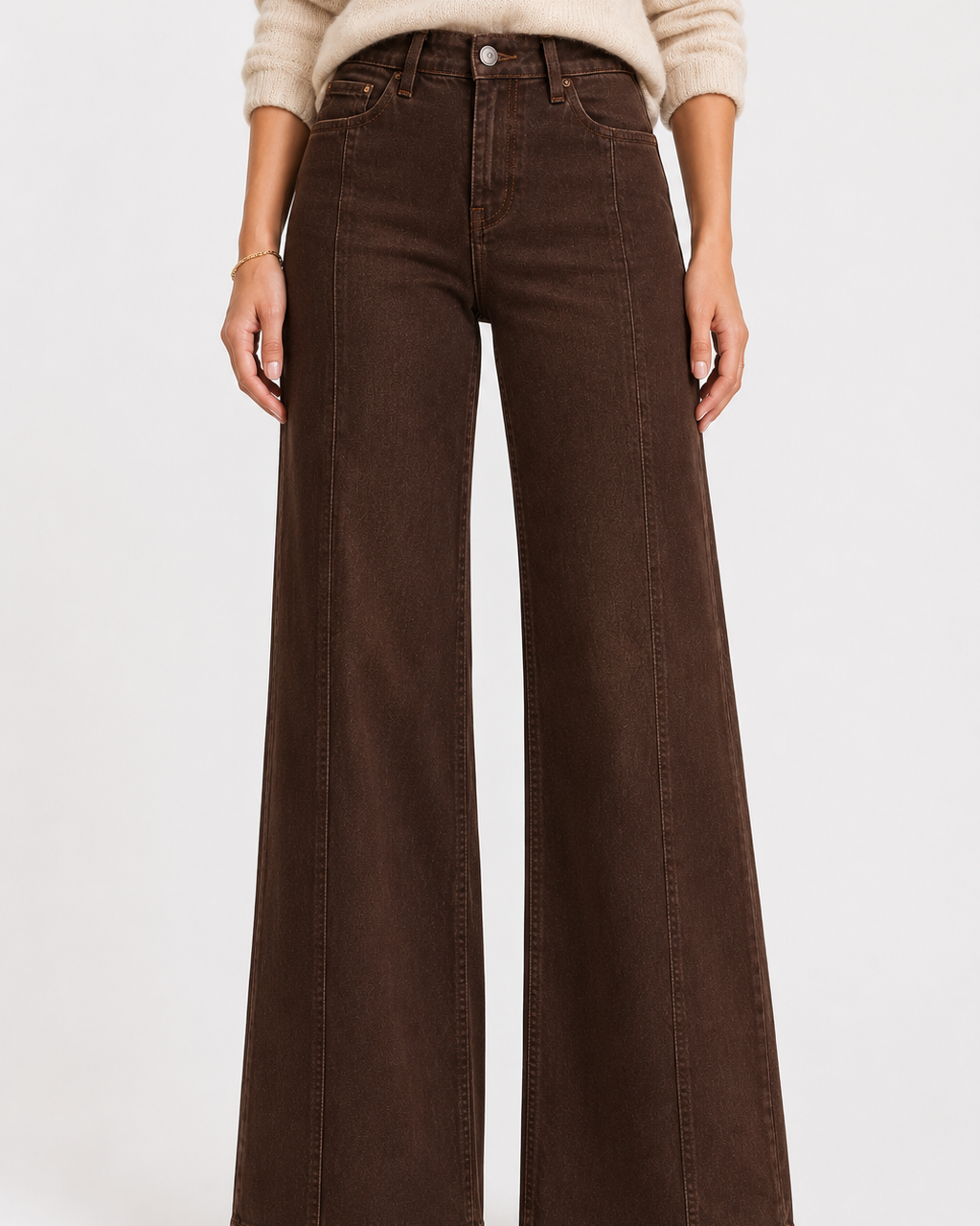 A person wearing dark brown wide-leg jeans with a beige sweater and beige pointed-toe heels, shown from the chest down against a light gray studio background.