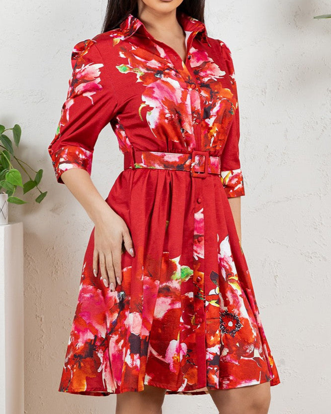 Woman wearing a red floral dress standing indoors with plants in the background