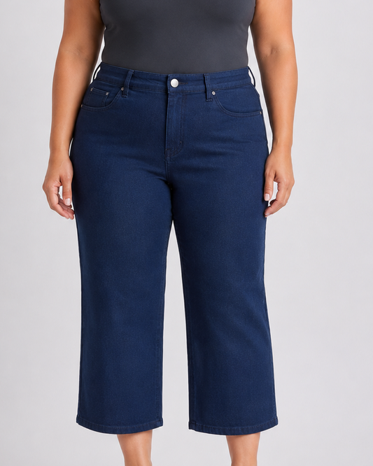 Woman wearing a dark gray tank top and blue jeans on a light gray background