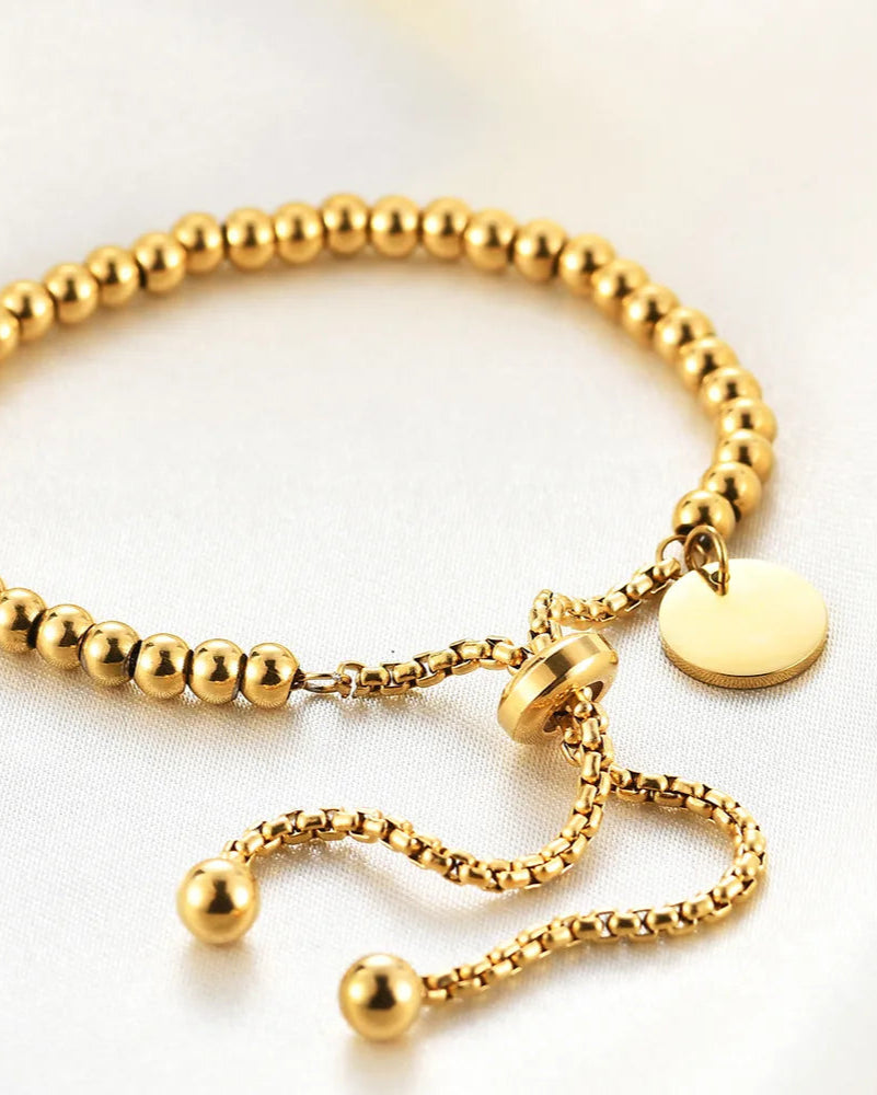 Gold beaded bracelet with a tag on a light background
