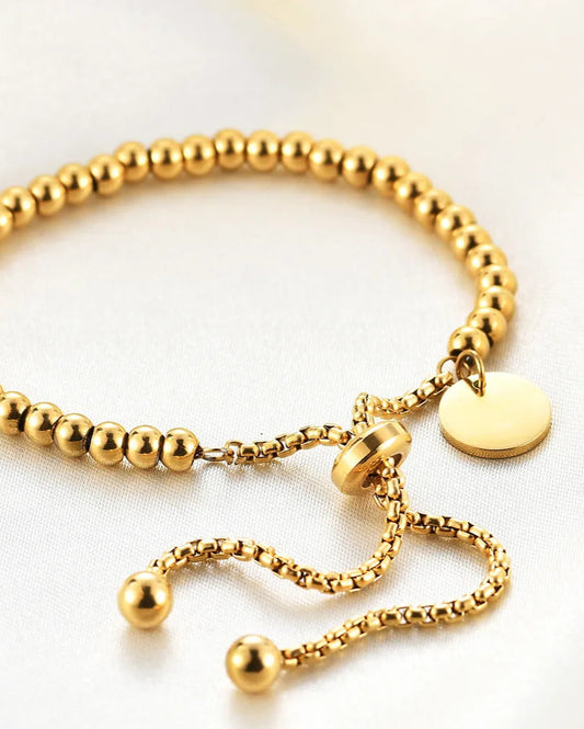 Gold beaded bracelet with a tag on a light background