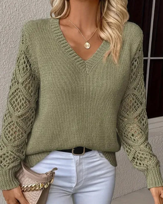 Person wearing a green knitted sweater and white pants, holding a beige handbag.