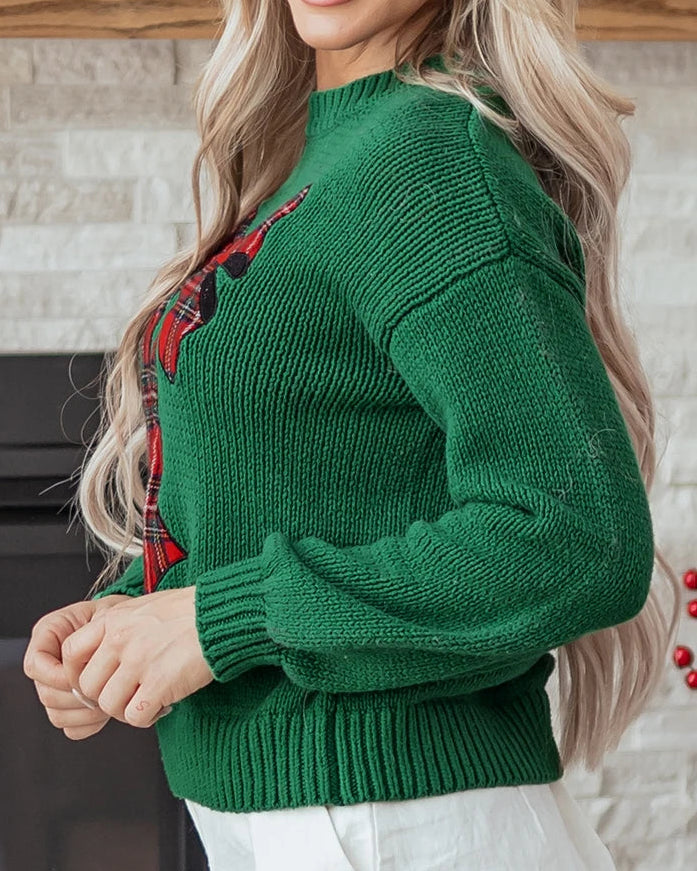 Woman wearing a green sweater with red accents in front of a decorated fireplace.