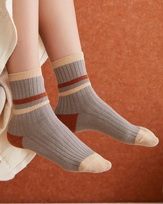 Person wearing gray socks with red and beige stripes on a warm-toned background